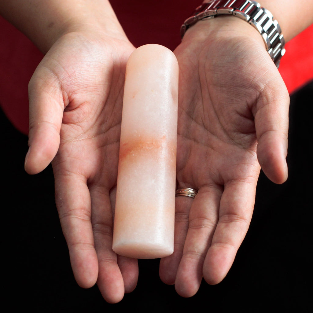 Pale pink salt deodorant stick with an orange band held across two open palms to show its size