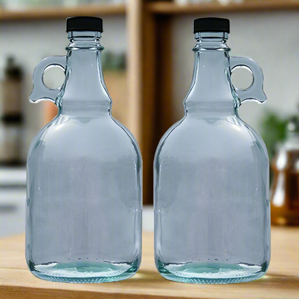 Two empty clear glass bottles with loop handles and black screw caps on a kitchen worktop