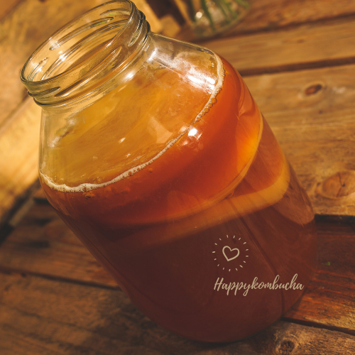 Open glass brewing jar filled with amber kombucha on a wooden table