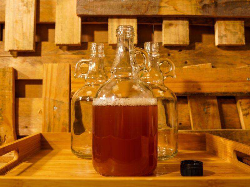 Three clear handled bottles on a wooden tray, the front bottle filled with amber drink and its cap beside it