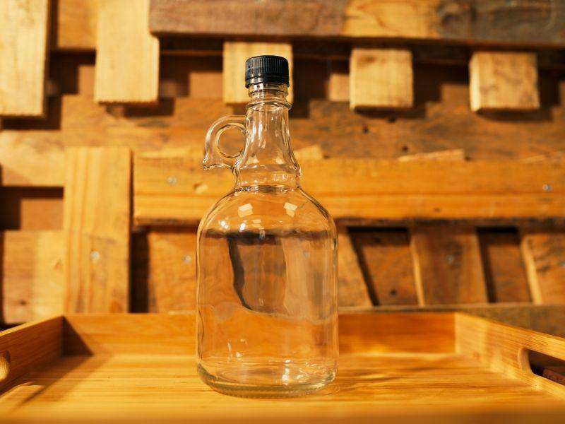 Clear glass handled bottle with a black screw cap on a wooden tray