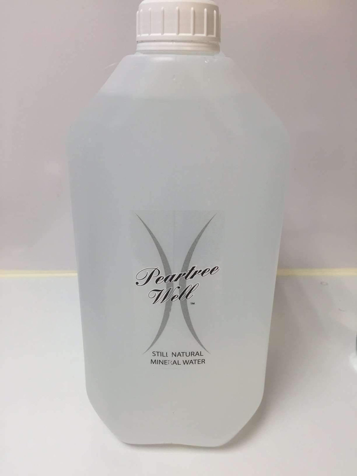 Front of a translucent container labelled Peartree Well Still Natural Mineral Water, with a white cap