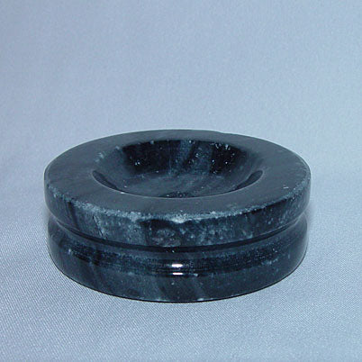 Round dark marble stand with a shallow central hollow on a pale blue background