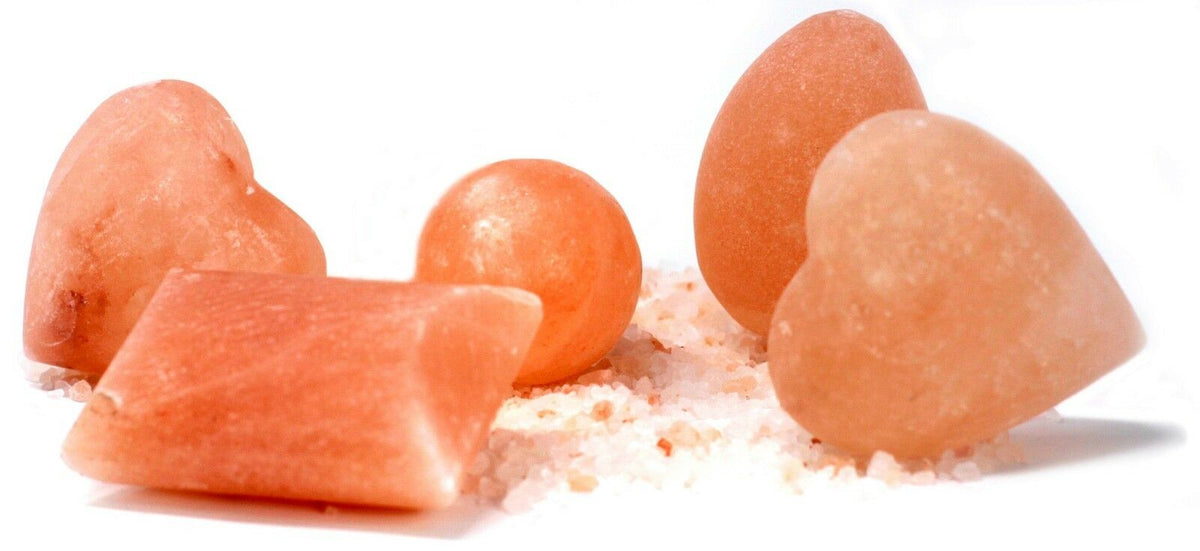 Pink Himalayan salt stones in heart, ball, egg and rectangular shapes arranged on coarse salt