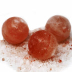Three rounded pink salt deodorant balls with pale natural markings on loose crystals